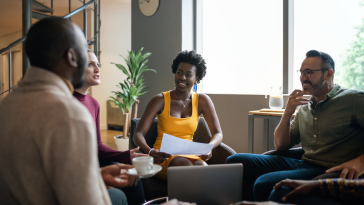 Group of young, smiling businesspeople talking together during a casual meeting in the lounge area of an office